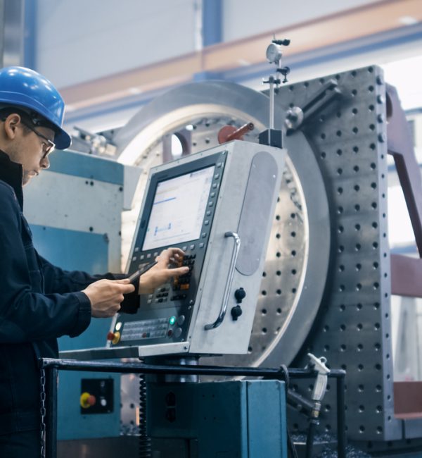 Factory worker is programming a CNC milling machine with a tablet computer.